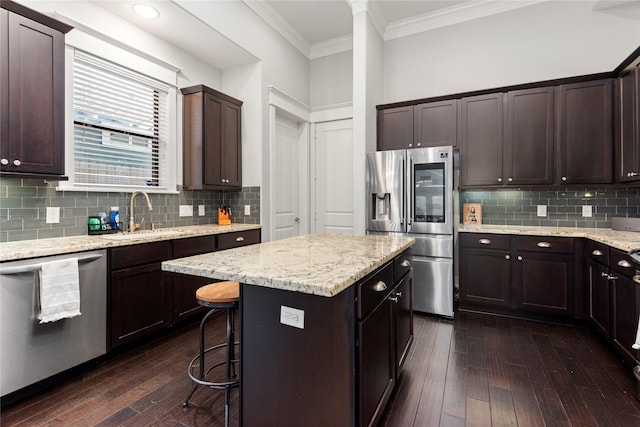 kitchen featuring dark wood-type flooring, sink, ornamental molding, appliances with stainless steel finishes, and a kitchen island