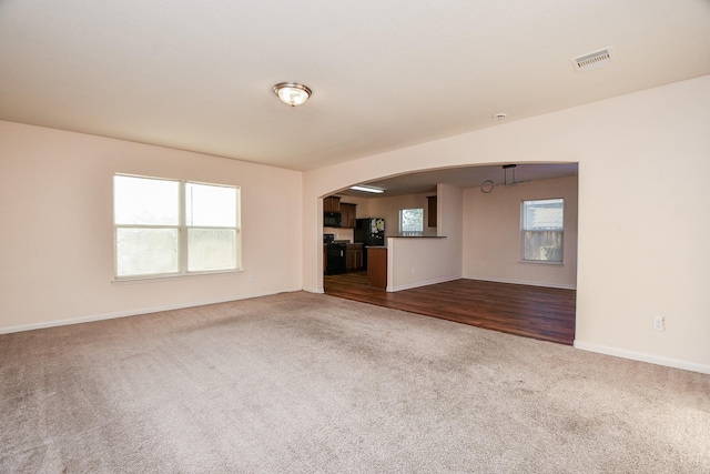 unfurnished living room featuring carpet, visible vents, arched walkways, and baseboards