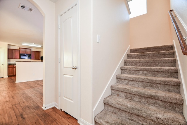 staircase featuring arched walkways, wood finished floors, visible vents, and baseboards