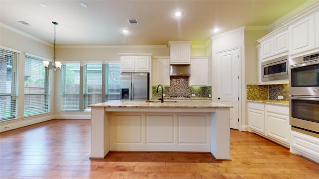 kitchen with appliances with stainless steel finishes, white cabinetry, hanging light fixtures, light stone counters, and an island with sink