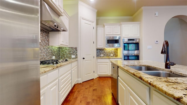 kitchen featuring sink, light stone counters, crown molding, light hardwood / wood-style flooring, and appliances with stainless steel finishes