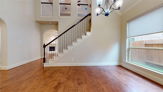 interior space featuring crown molding, a towering ceiling, an inviting chandelier, and hardwood / wood-style floors