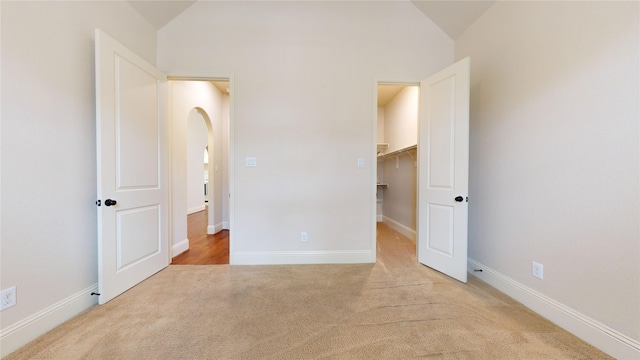 unfurnished bedroom featuring lofted ceiling, a walk in closet, and light carpet