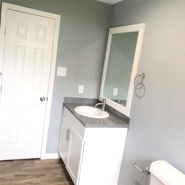 bathroom with baseboards, vanity, toilet, and wood finished floors