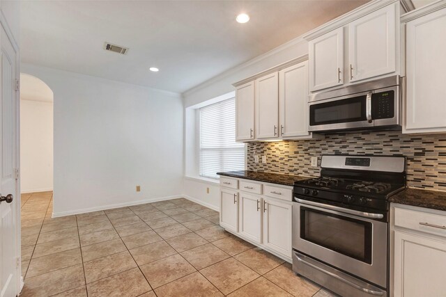 kitchen featuring white cabinetry, stainless steel appliances, decorative backsplash, and dark stone countertops