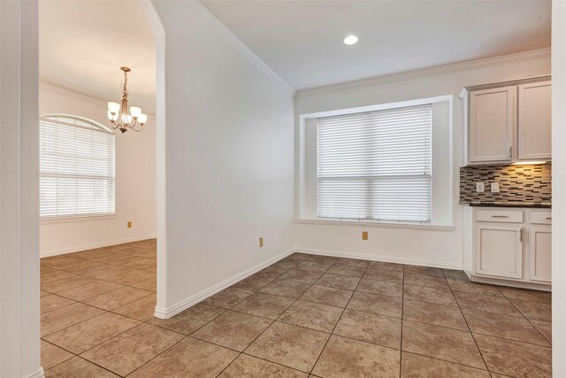 unfurnished dining area with ornamental molding, light tile patterned floors, and an inviting chandelier