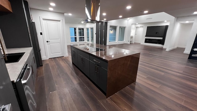 kitchen featuring black electric cooktop, island range hood, dark hardwood / wood-style floors, and a center island with sink