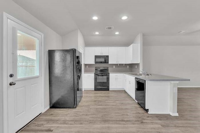 kitchen with light hardwood / wood-style flooring, kitchen peninsula, white cabinets, and black appliances