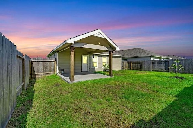 back house at dusk featuring a patio and a yard