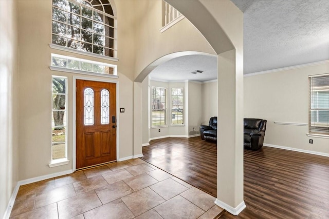 foyer entrance featuring crown molding, arched walkways, a textured ceiling, and wood finished floors