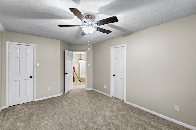 unfurnished bedroom with light carpet, ceiling fan, a textured ceiling, and baseboards