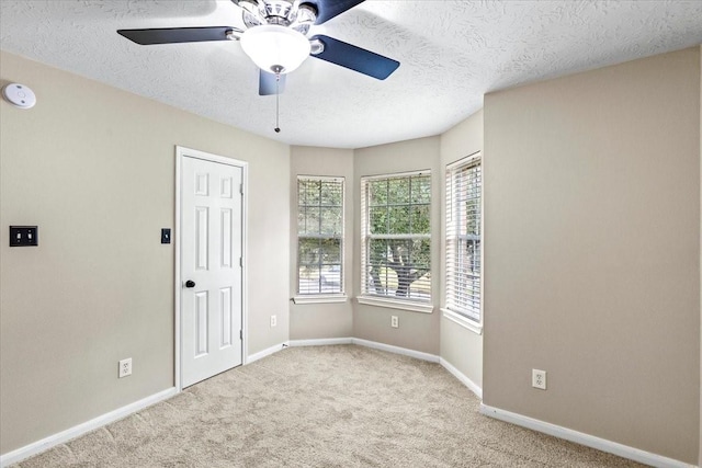 unfurnished room featuring light carpet, ceiling fan, baseboards, and a textured ceiling