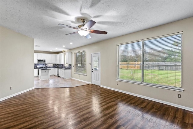 unfurnished living room with a ceiling fan, a textured ceiling, baseboards, and wood finished floors