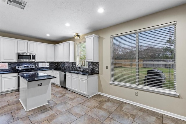 kitchen featuring stainless steel appliances, visible vents, white cabinetry, a center island, and dark countertops