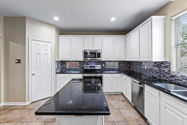 kitchen with appliances with stainless steel finishes, white cabinets, a kitchen island, a sink, and dark stone counters