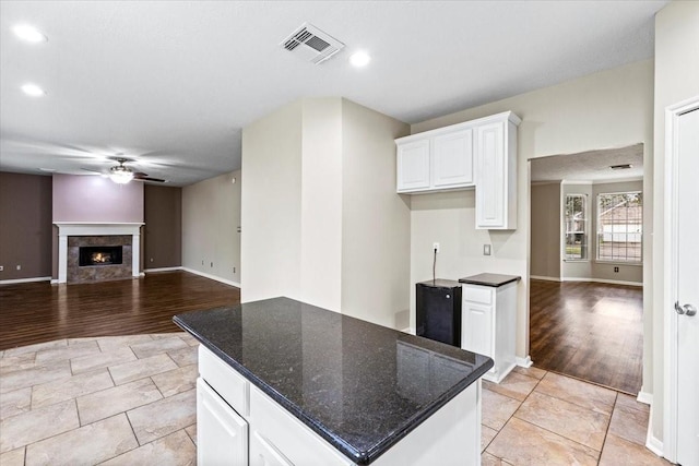 kitchen with a warm lit fireplace, visible vents, dark stone counters, white cabinets, and open floor plan