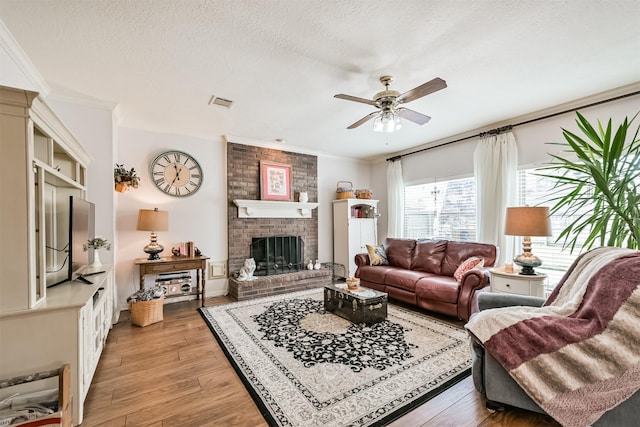 living room featuring ornamental molding, a brick fireplace, a textured ceiling, and light wood-type flooring