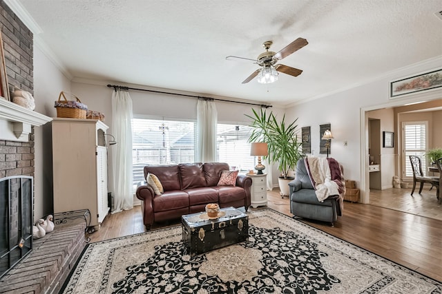 living room with ceiling fan, hardwood / wood-style floors, ornamental molding, a textured ceiling, and a brick fireplace