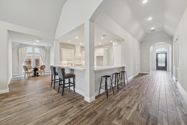 kitchen featuring lofted ceiling, hardwood / wood-style flooring, white cabinetry, a kitchen bar, and kitchen peninsula