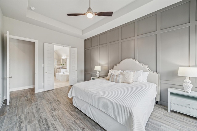 bedroom with ceiling fan, connected bathroom, a tray ceiling, and light hardwood / wood-style floors