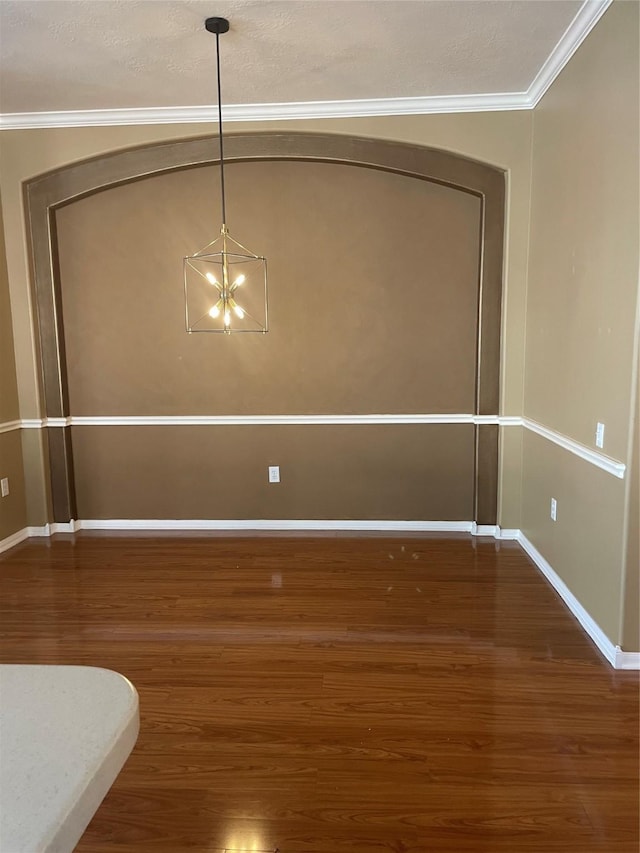 unfurnished dining area featuring a notable chandelier, baseboards, wood finished floors, and crown molding