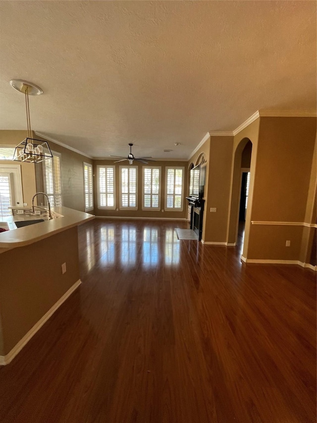 unfurnished living room with a textured ceiling, baseboards, dark wood finished floors, and crown molding