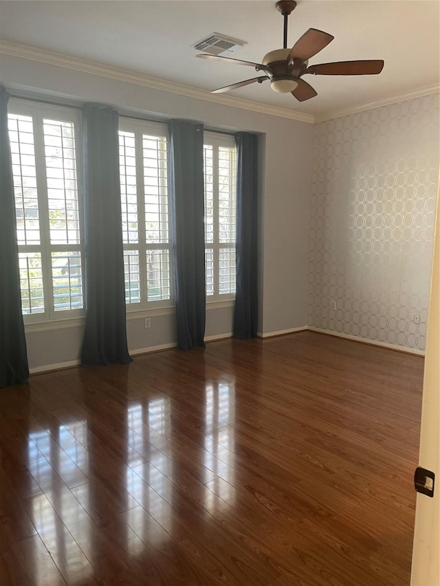 empty room with ceiling fan, wood finished floors, visible vents, baseboards, and crown molding