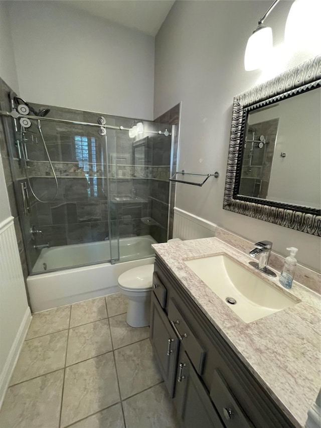 full bath with toilet, a wainscoted wall, tile patterned flooring, combined bath / shower with glass door, and vanity