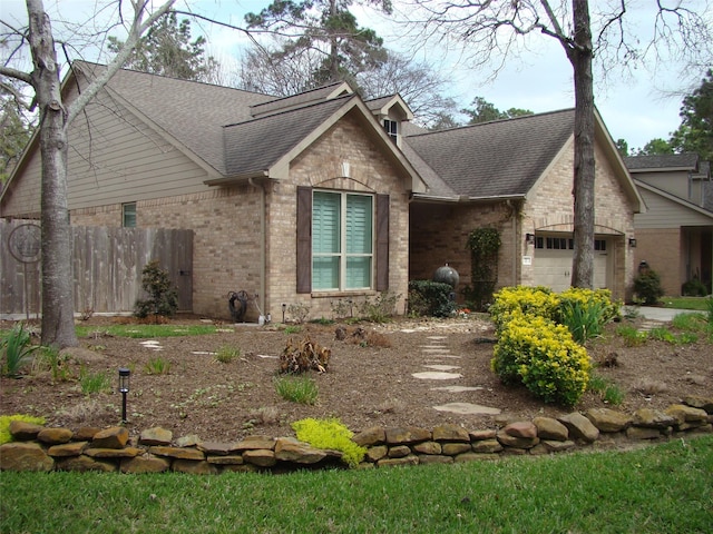 view of front of home with brick siding, roof with shingles, an attached garage, and fence