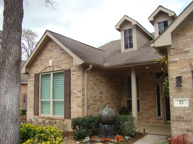 exterior space featuring brick siding and a shingled roof