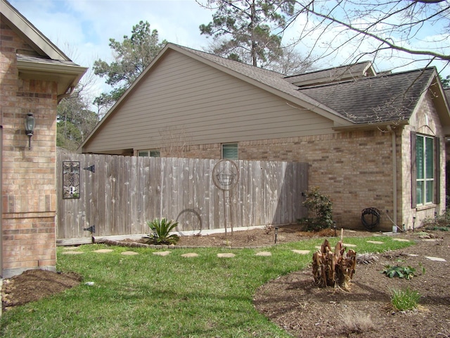 view of side of property with a yard, brick siding, fence, and a shingled roof