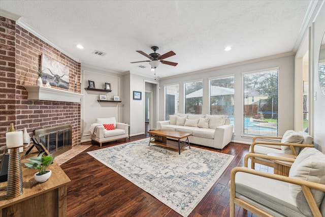 living area with dark wood-type flooring, a brick fireplace, visible vents, and crown molding