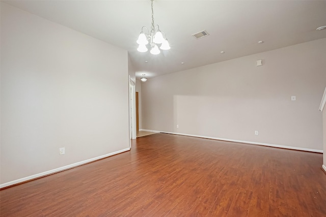 spare room featuring wood-type flooring and a chandelier