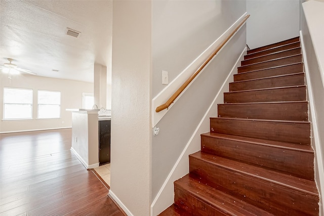 staircase with hardwood / wood-style flooring, a textured ceiling, and ceiling fan