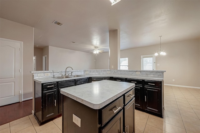 kitchen featuring sink, a center island, hanging light fixtures, light tile patterned floors, and ceiling fan with notable chandelier