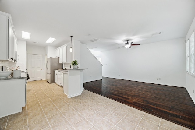 kitchen with a skylight, stainless steel fridge, pendant lighting, ceiling fan, and white cabinets