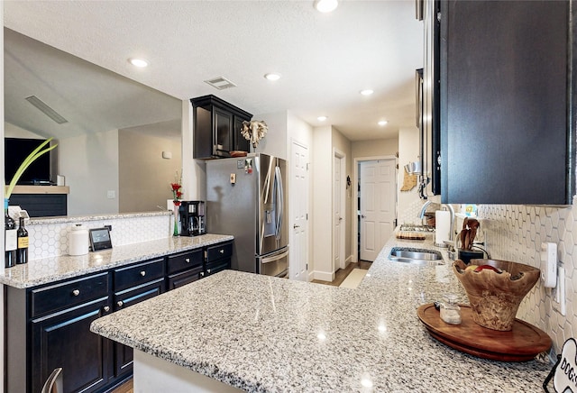 kitchen featuring light stone countertops, kitchen peninsula, backsplash, and stainless steel fridge with ice dispenser