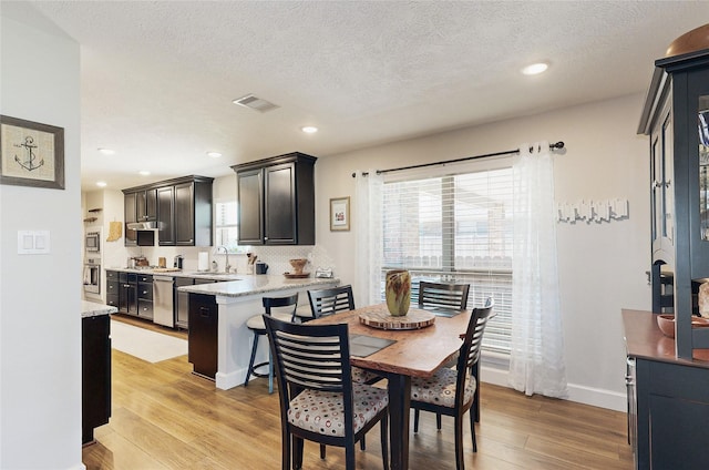 dining space featuring sink, a textured ceiling, and light wood-type flooring