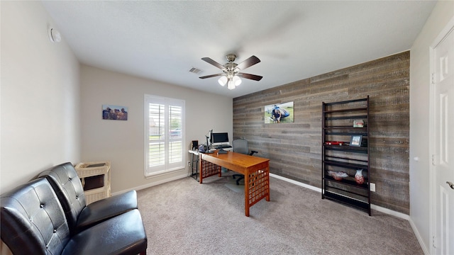 carpeted office space featuring ceiling fan and wooden walls