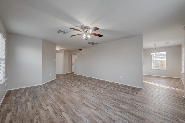 empty room featuring ceiling fan with notable chandelier and light wood-type flooring