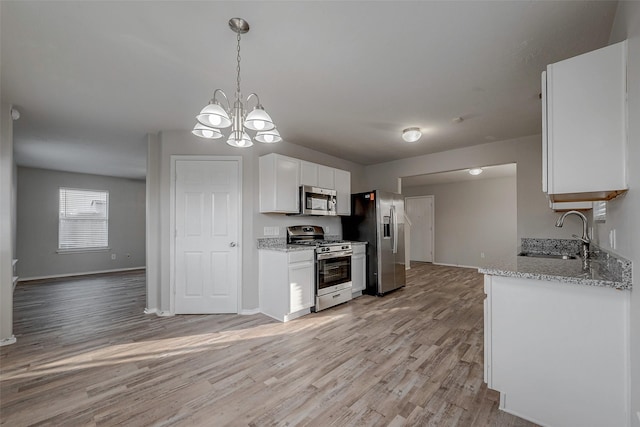 kitchen with sink, appliances with stainless steel finishes, light stone countertops, white cabinets, and decorative light fixtures