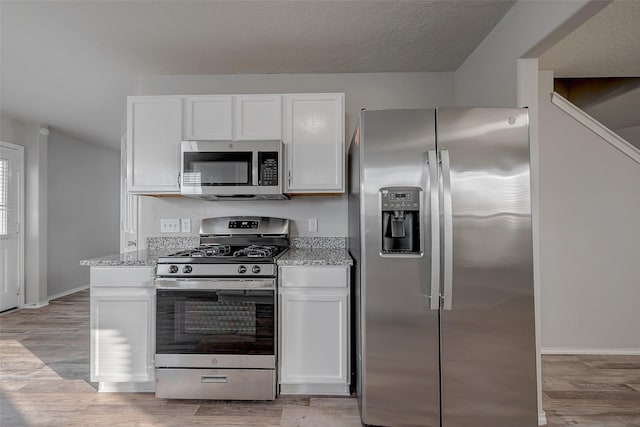 kitchen featuring stainless steel appliances, light stone countertops, white cabinets, and light hardwood / wood-style flooring