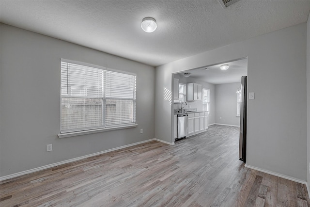 unfurnished living room featuring sink, a textured ceiling, and light wood-type flooring