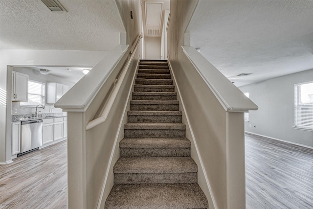 staircase featuring wood-type flooring, plenty of natural light, sink, and a textured ceiling