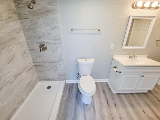 bathroom with a tile shower, hardwood / wood-style floors, vanity, and toilet