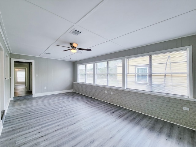 empty room featuring ceiling fan, brick wall, and wood-type flooring