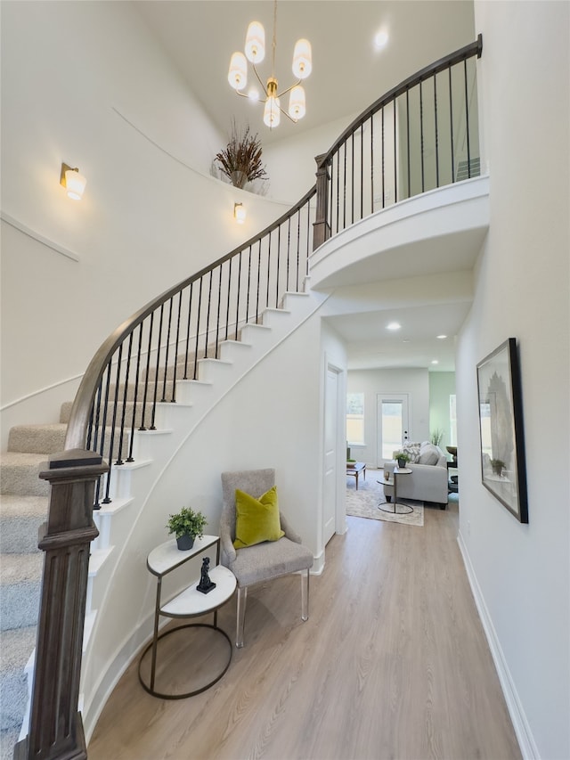 stairs with a notable chandelier, a high ceiling, baseboards, and wood finished floors