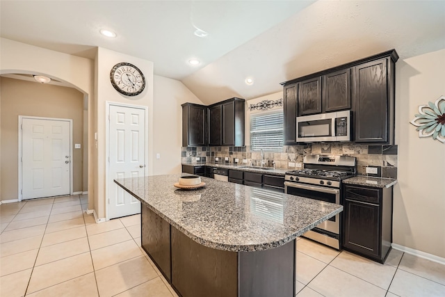 kitchen featuring light tile patterned flooring, tasteful backsplash, a center island, appliances with stainless steel finishes, and dark stone counters