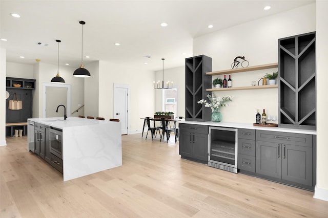 kitchen featuring pendant lighting, sink, beverage cooler, light stone countertops, and light hardwood / wood-style flooring