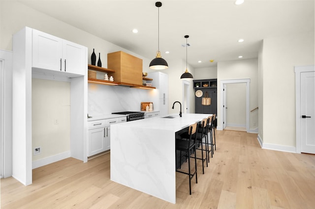 kitchen with decorative backsplash, an island with sink, white cabinets, decorative light fixtures, and light wood-type flooring